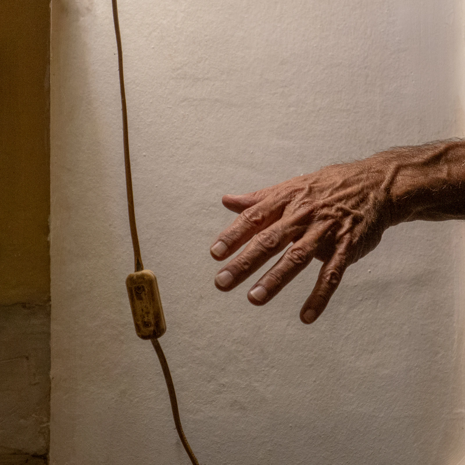 An older hand reaching for a light switch on a wall