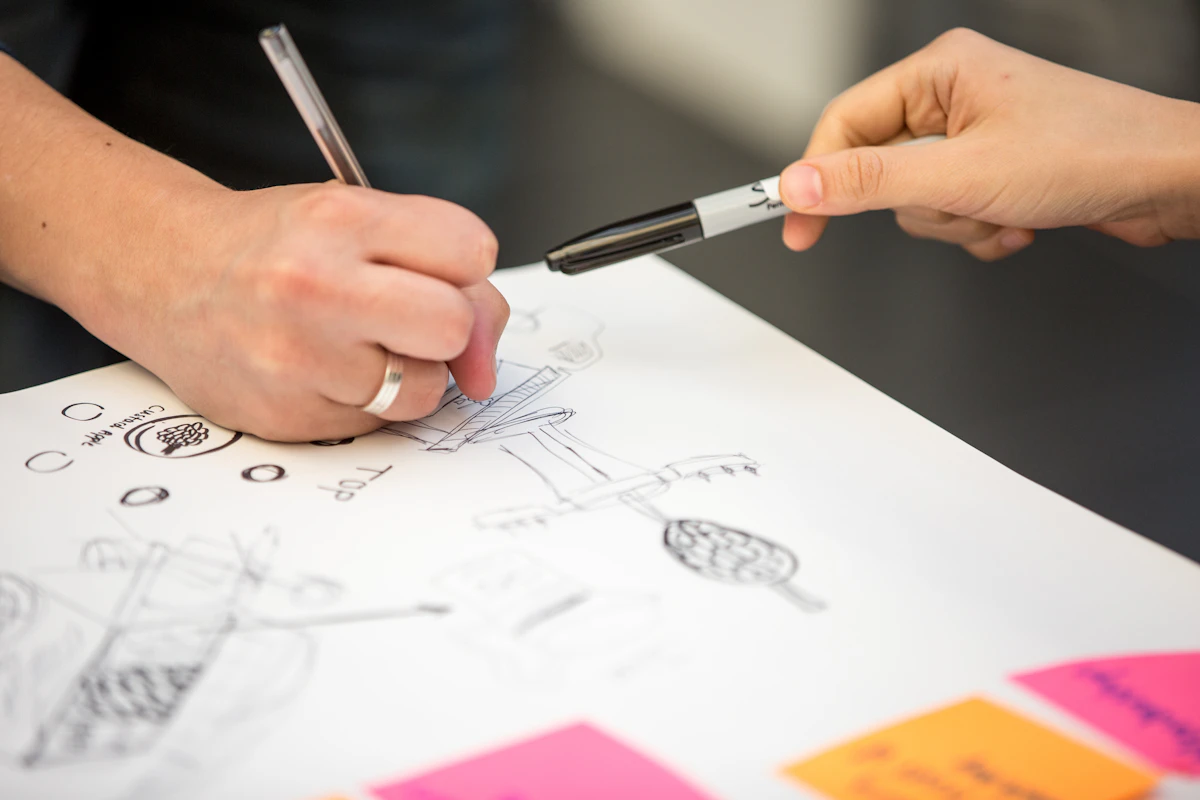 A hand sketching layouts on paper beside sticky notes