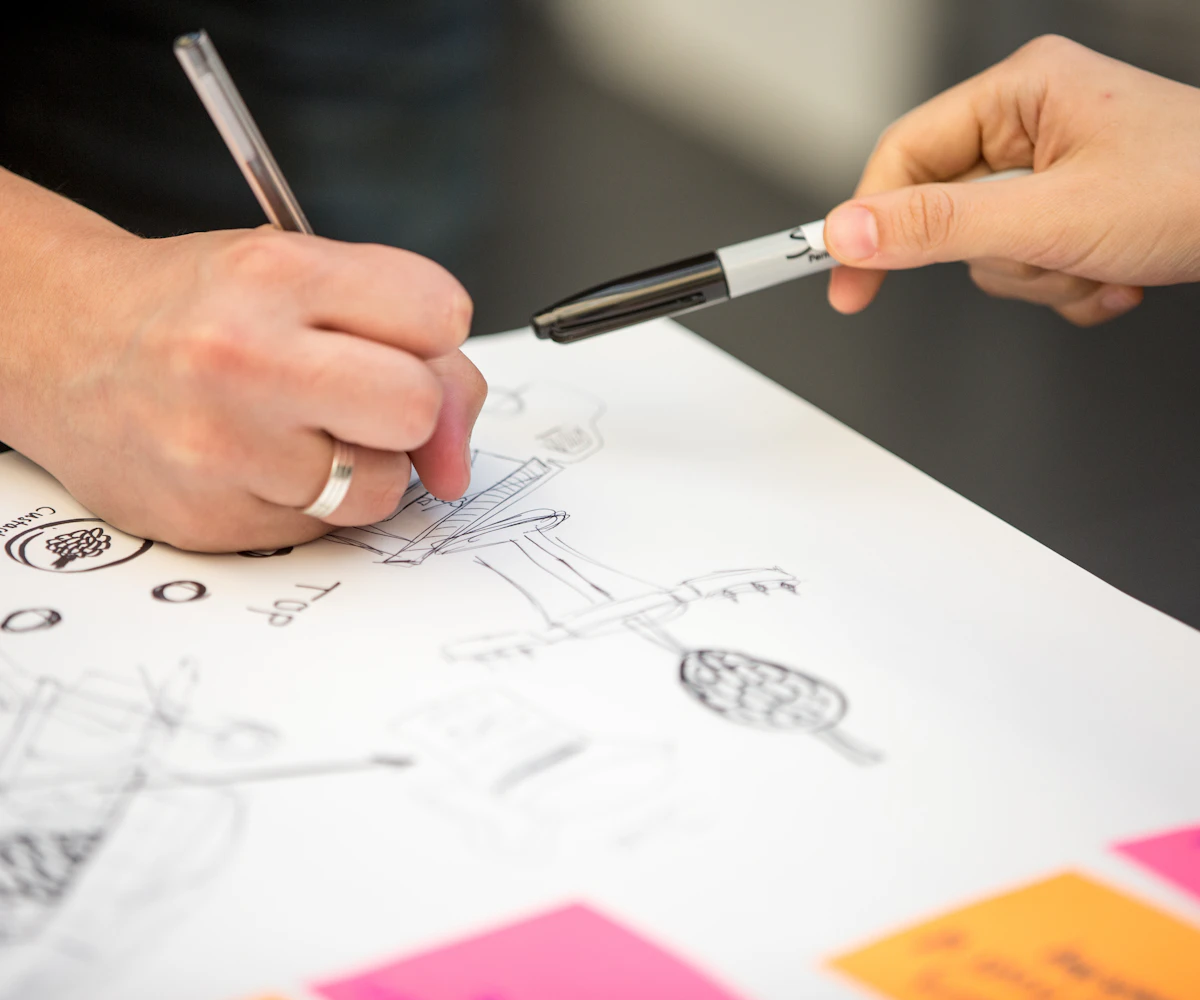 A hand sketching layouts on paper beside sticky notes